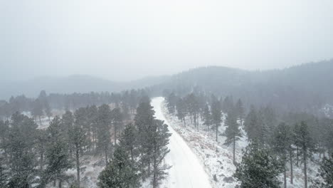 Imágenes-Aéreas-De-Drones-Sobre-Una-Carretera-Rural-Cubierta-De-Nieve-Rodeada-De-Pinos-Cerca-De-La-Montaña-Flatirons-En-Boulder,-Colorado,-EE.UU.-Durante-Una-Tormenta-De-Nieve-Nevada