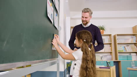 side view of a teacher in front of the blackboard in english classroom, then a female student stands up and sticks a paper with the words 'happy' and 'sad' on blackboard