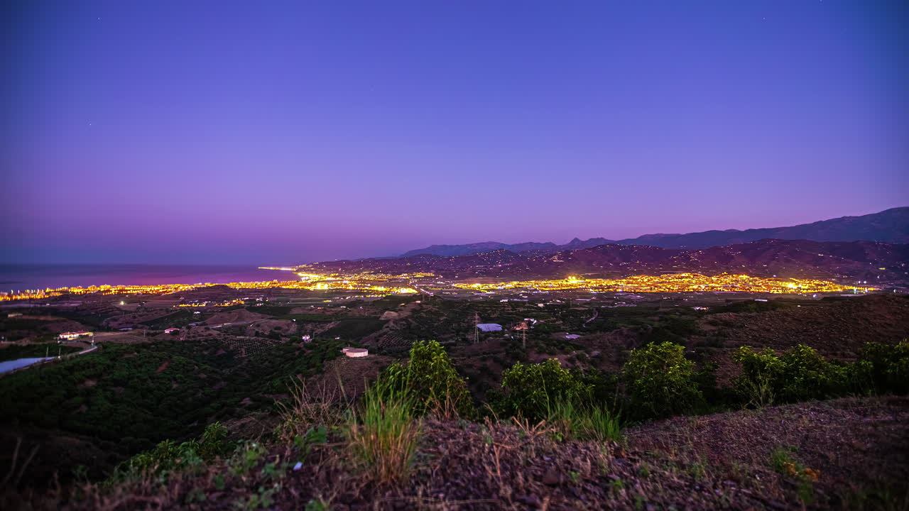 timelapse del crepúsculo vista del paisaje urbano con luces brillantes a medida que cae la noche sobre la extensa ciudad y la costa cercana