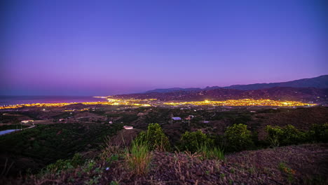 timelapse del crepúsculo vista del paisaje urbano con luces brillantes a medida que cae la noche sobre la extensa ciudad y la costa cercana