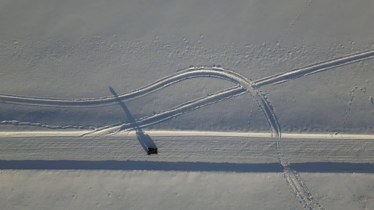 la parte superior aérea hacia abajo sigue el vehículo atv que conduce a lo largo de la carretera cubierta de nieve, proyectando una larga sombra