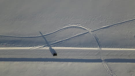 aerial top down follows atv vehicle driving along snow-covered road, casting long shadow