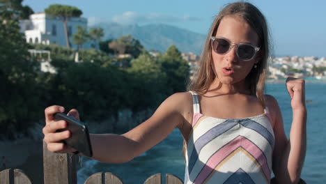 chica alegre haciendo muecas al teléfono inteligente al aire libre. adolescente alegre posando para la cámara.
