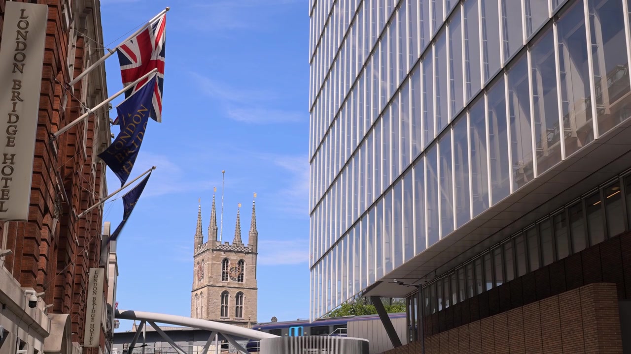 Southwark Katedralens tårn rejser sig mellem London Bridge Hotels flag og en glas kontorfacade på en klar sommerdag