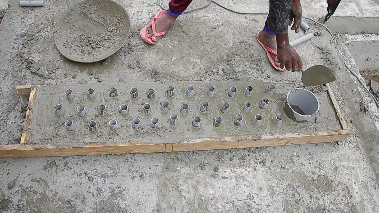 Indian mason worker placing concrete wet mix around pipes in preparation for leveling and finishing the slab