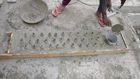 indian mason worker placing concrete wet mix around pipes in preparation for leveling and finishing the slab