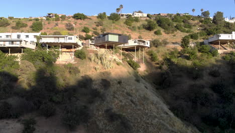 aerial flyby of homes on stilts hanging off cliffs of a mountain overlooking a valley city