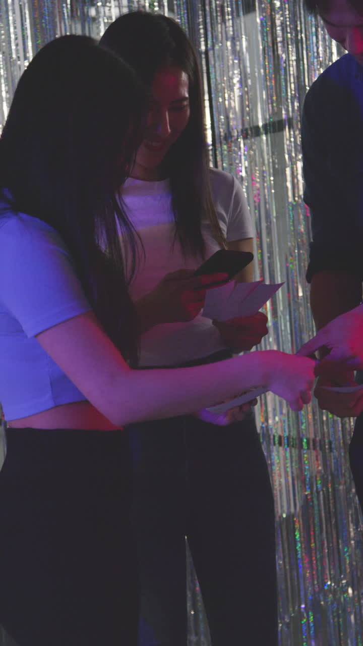 video vertical de un grupo de amigos tomando selfies divirtiéndose mirando las impresiones de la cabina de fotos en un club nocturno o feria 1