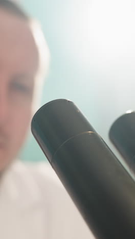 una vista de cerca de un técnico usando un microscopio en un laboratorio, el primer plano muestra las lentes del microscopio mientras colocaba sus ojos en el microscopio, con la luz encendida detrás de él