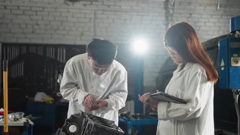 two inventors in chinese automotive workshop, boy showing reading to girl while she records data on tablet, he measures engine component again under bright light illuminating scene