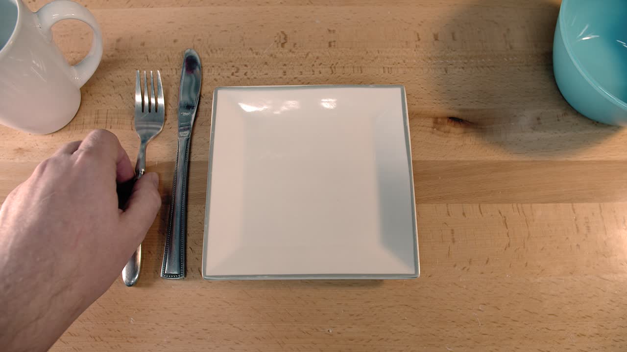 alguien pone una mesa con utensilios y platos