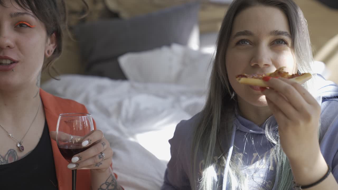 집에서 바닥에 앉아 와인을 마시고, 피자를 먹고, 웃는 두 명의 행복한 소녀들