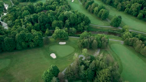 aerial birds-eye view of golf course fairway and putting green, natural grass, sand bunkers and river at sunset