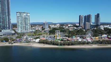 oceanside carnival set-up along a coastal beach strip below a towering city landscape