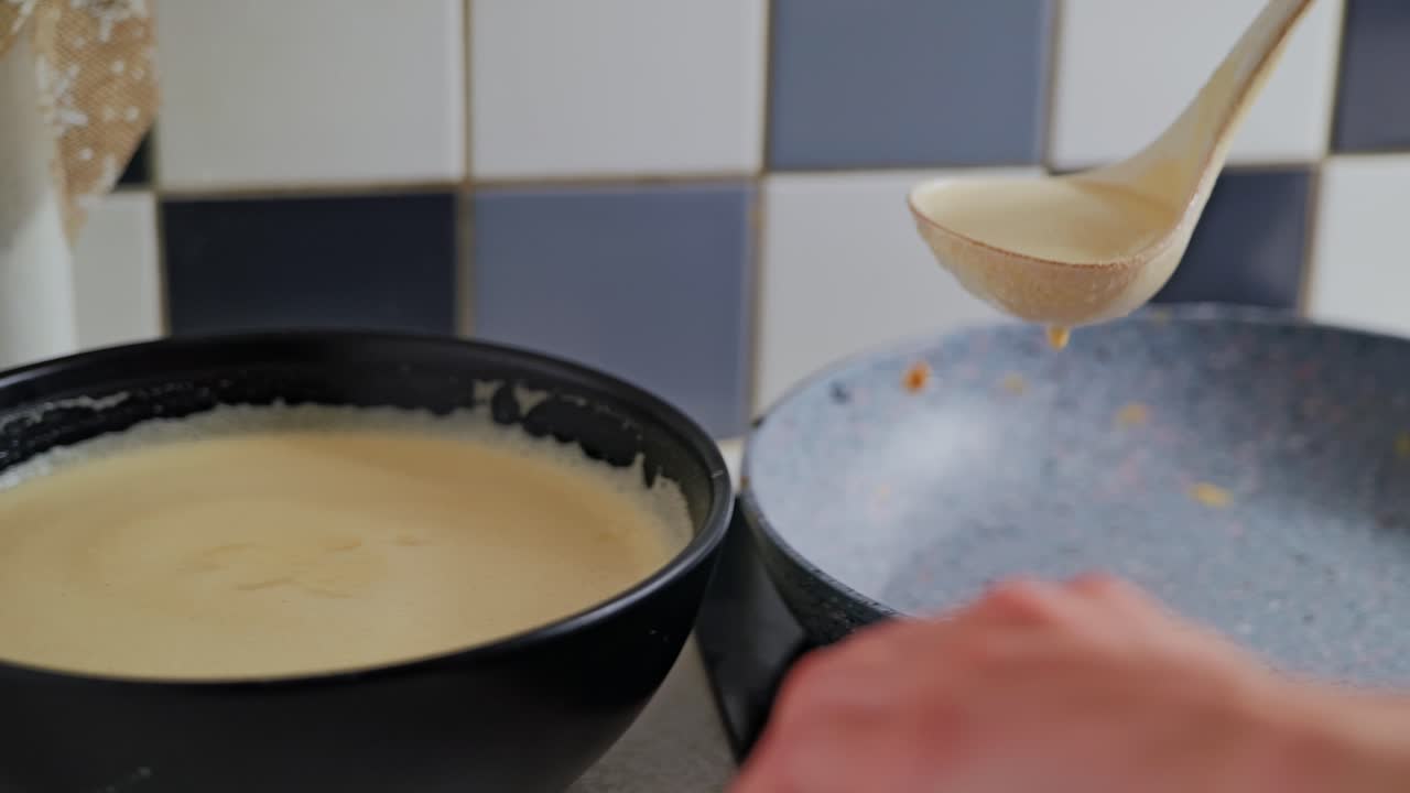 Smooth pancake batter drips gently from ladle in calm slow motion kitchen moment
