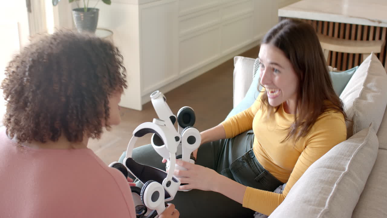 women friends sitting on couch, discussing and holding VR headsets in living room