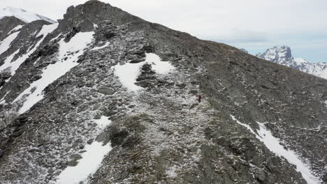 Cinematic-revealing-drone-shot-of-someone-hiking-up-mountain-ridge-in-the-snow-covered-Caucasus-Mountains-in-Georgia