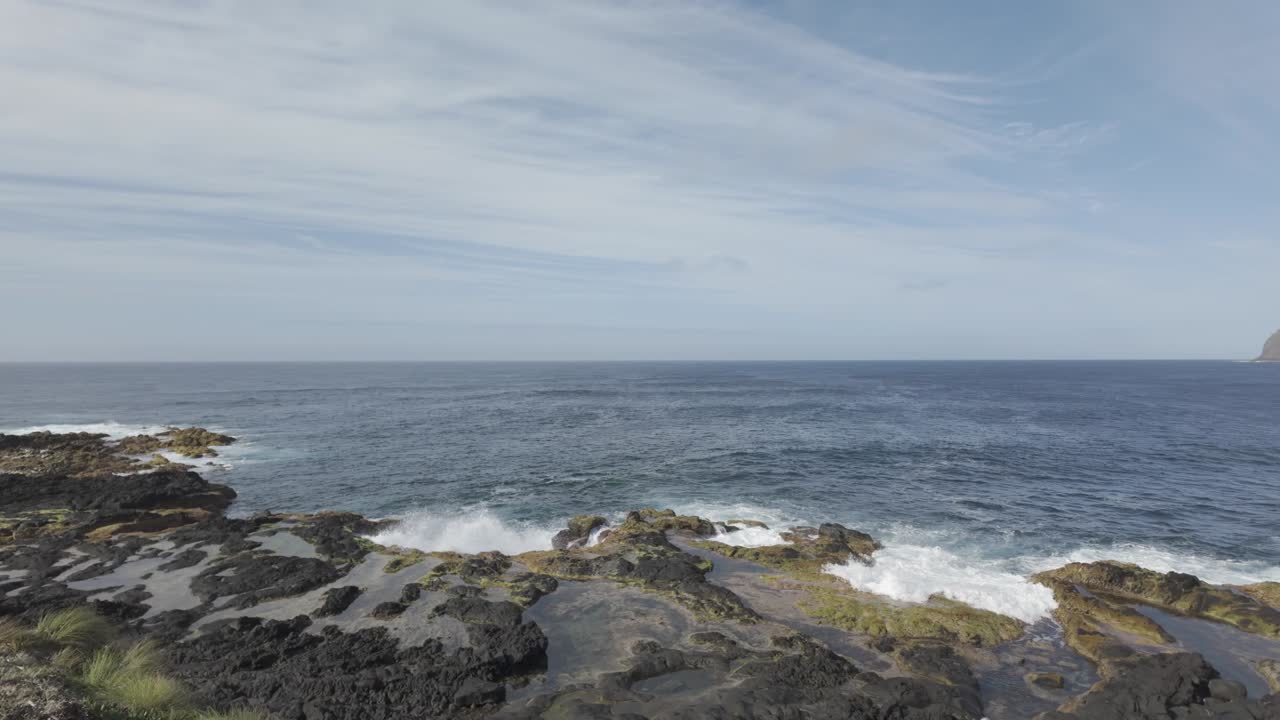 Garis pantai berbatu Mosteiros, Sao Miguel di bawah langit biru dengan awan yang tersebar, ombak menghantam pantai.