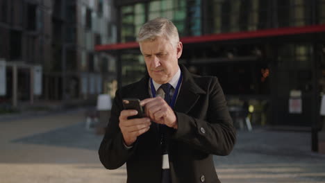 portrait-of-executive-businessman-texting-networking-using-smartphone-browsing-app-looking-serious-pensive-in-urban-city