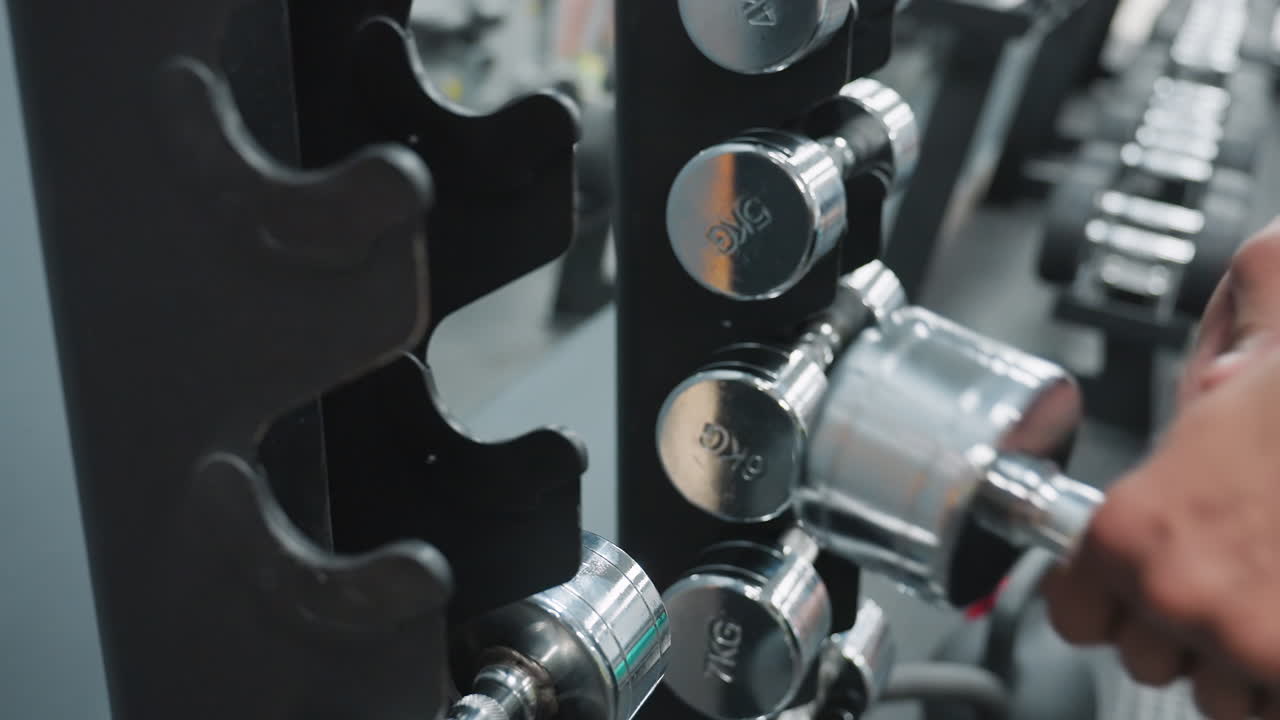 close up partial view of person returning shiny 5kg chrome dumbbell to weight rack inside gym, surrounded by other neatly arranged dumbbells, reflecting workout discipline
