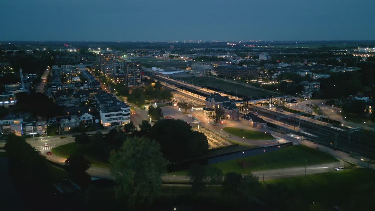 Night aerial view of Woerden featuring the railway station, illuminated roads, moving traffic and urban infrastructure in a Dutch city at night