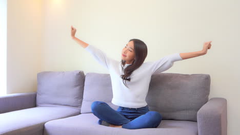 young asian female stretching her hand while sitting on couch in a family room