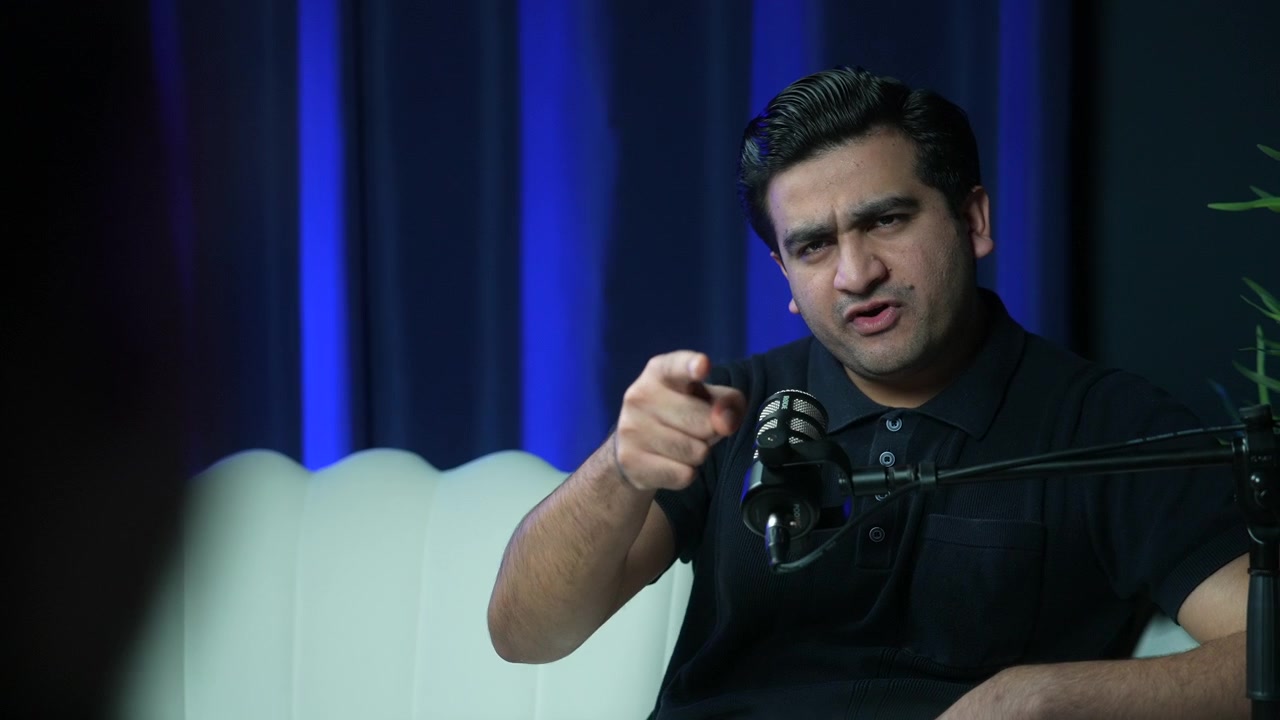 Podcast host gesturing while speaking in modern recording studio, animated pointing back and forth with guest responding gestures