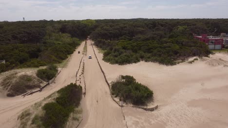 Luftaufnahme-Des-Fahrzeugs,-Das-An-Einem-Sonnigen-Tag-Am-Strand-Auf-Einem-Sandigen-Weg-Zwischen-Wäldern-Fährt