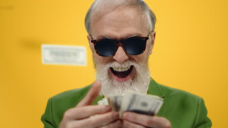 happy aged man counting money in studio. cheerful guy throwing dollars indoors.