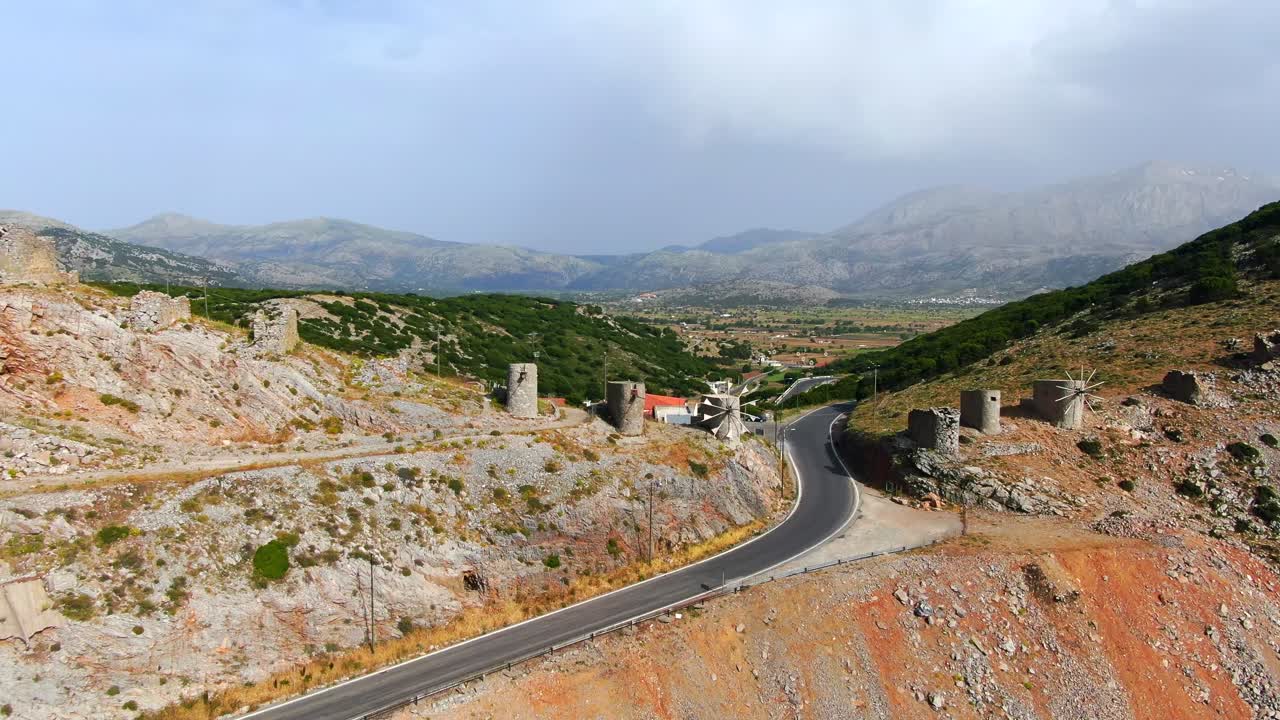 Ancient windmills stand in the mountains edge. Flyover aerial shot. Island Spinalonga, Crete, Greece