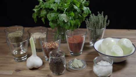 Close-up-of-a-wooden-table-with-parsley,-onion,-pepper,-thyme,-garlic,-cayenne-pepper,-and-rosemary,-the-ingredients-for-cafe-paris-butter