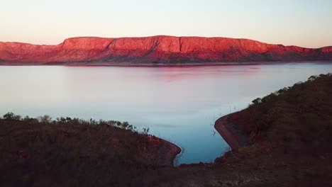 spectacular fast aerial fly-over of car on mountain top beside huge lake at sunset with red mountains in background