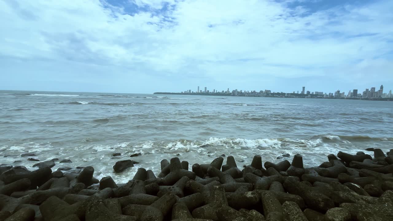 Sea waves crashing the shore of marine drive mumbai with view of city in background