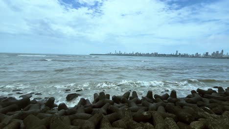 sea waves crashing the shore of marine drive mumbai with view of city in background
