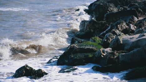 The-sea-waves-crash-into-a-rocky-seashore-with-green-moss
