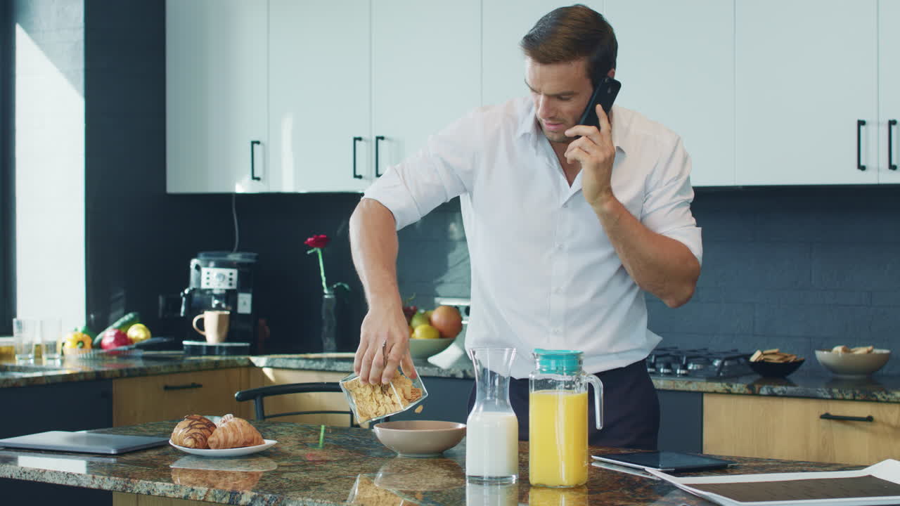 hombre feliz preparando el desayuno en la cocina. persona relajada hablando por teléfono.