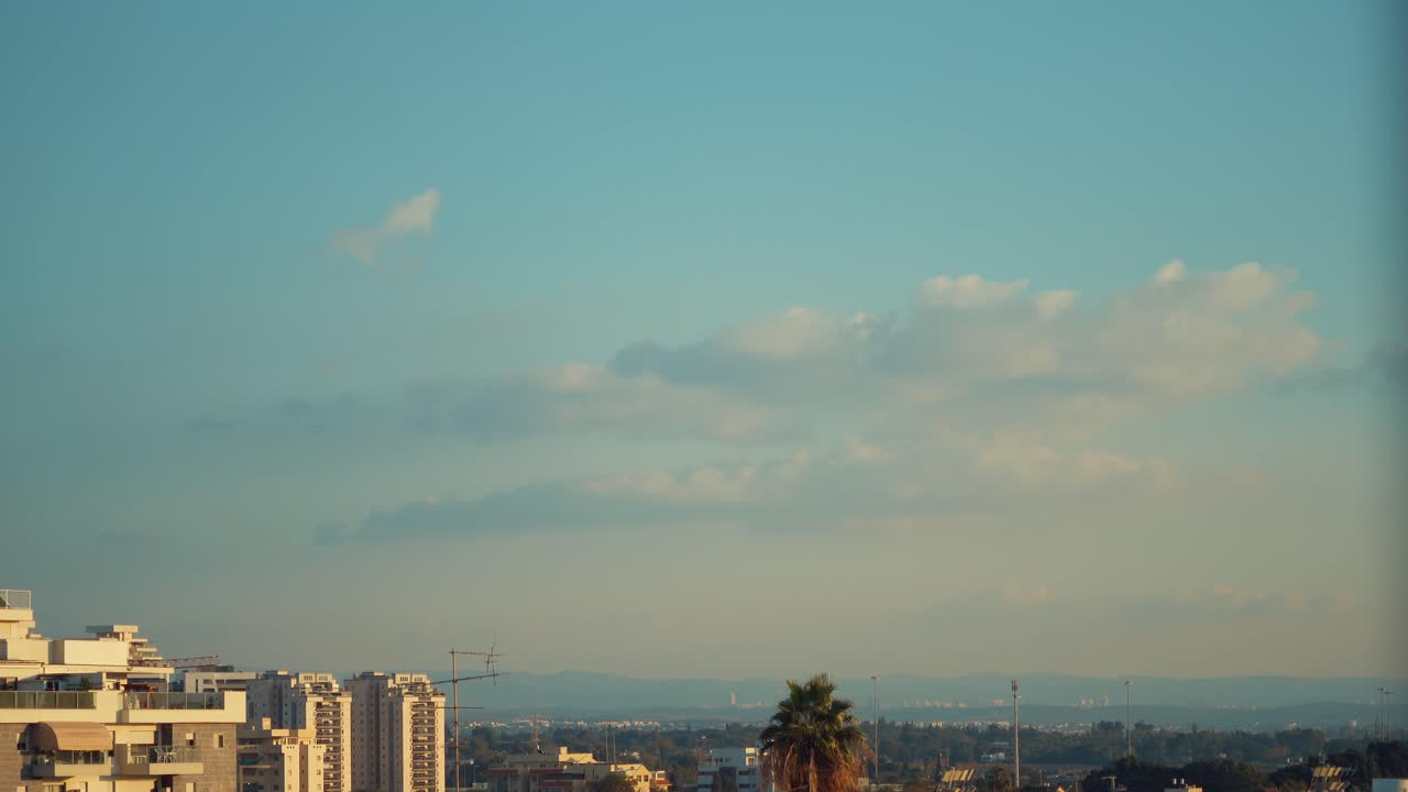 Vídeo em time-lapse acelerado de nuvens em movimento nos céus azuis, árvore verde, paisagem urbana e uma palmeira ao fundo, Vídeo 4K