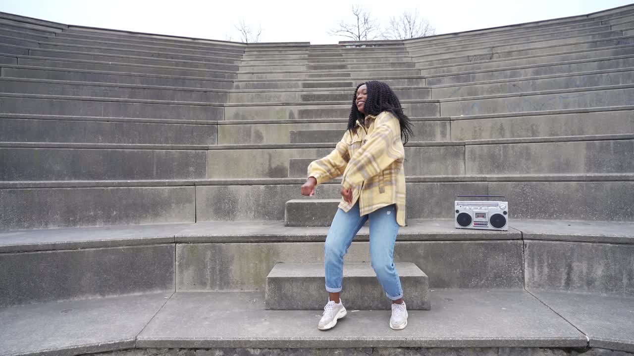 Smiling black woman dancing on steps in park
