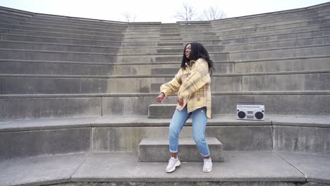 Smiling-black-woman-dancing-on-steps-in-park