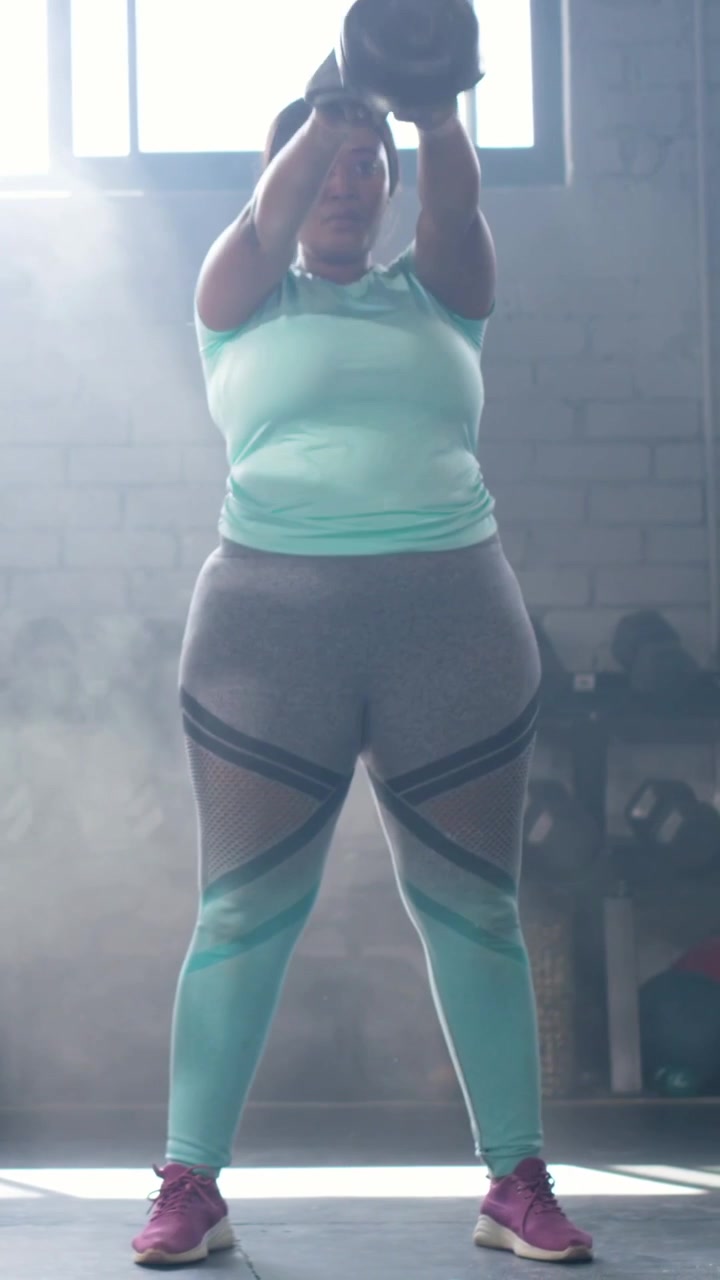 Video verticale: Donna esegue oscillazioni con kettlebell dal petto in studio per allenare la forza, con un top color menta.