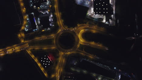 Zoom-out-overhead-drone-view-of-a-roundabout-and-highway-by-night