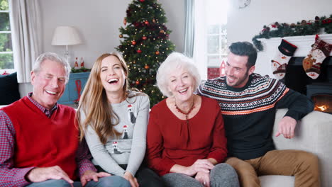 Portrait-Of-Senior-Parents-With-Adult-Offspring-Wearing-Festive-Jumpers-Sitting-On-Sofa-In-Lounge-At-Home-On-Christmas-Day