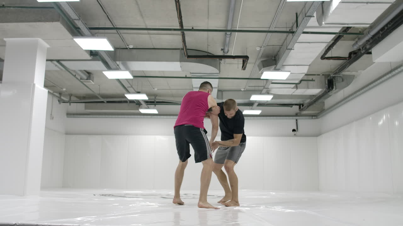 dos luchadores masculinos en una habitación blanca trabajan lanzando esteras. toma un agarre y lanza a través de ti mismo.