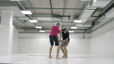 two male wrestlers in a white room work out throwing mats. take a grapple and throw through yourself.