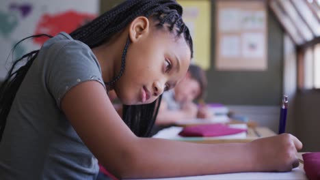 chica escribiendo en un libro mientras estaba sentada en su escritorio en la escuela
