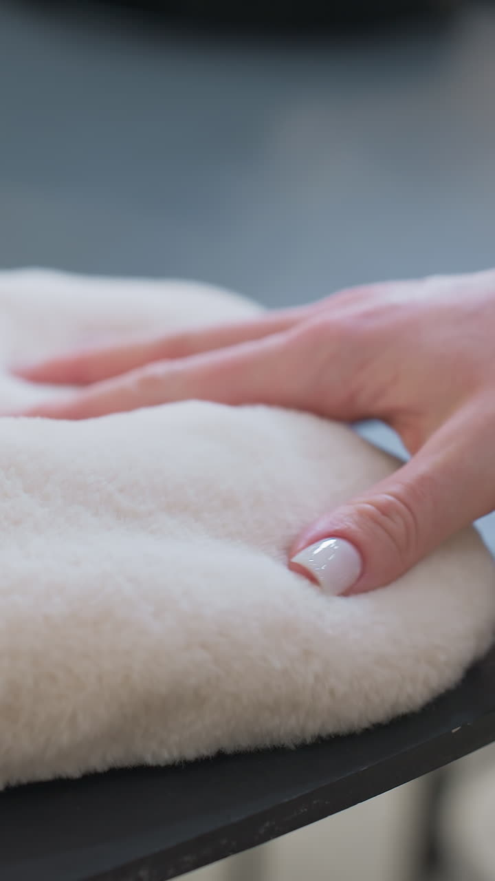 Close-up of white winter gloves resting on a dark surface as a hand reaches to pick them up, cozy, warm textures with a blurred background