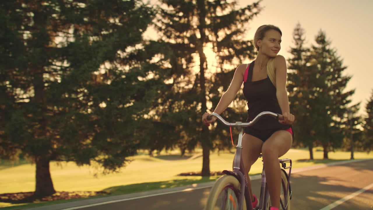 금빛 해가 지는 풍경에서 여름 공원에서 자전거를 타고 있는 피트니스 여성