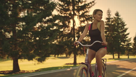 Mujer-Fitness-Montando-Bicicleta-En-El-Parque-De-Verano-En-El-Paisaje-Dorado-Del-Atardecer