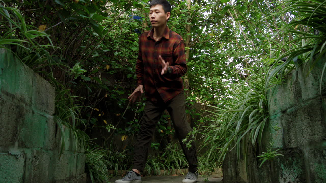 재능있는 아시아인 숙련된 남자가 정글 환경에서 프리스타일 댄스 단계를 연습하고 있습니다.