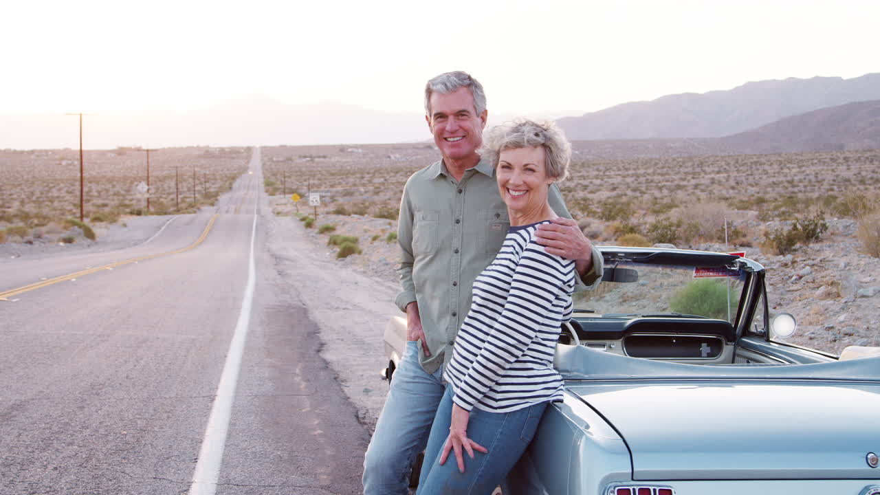 Pareja mayor de viaje por carretera de pie junto al coche sonriendo a la cámara